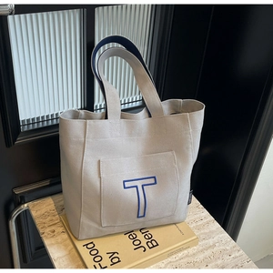 Detailed embroidery of a blue T letter on a beige canvas tote bag with contrast handles