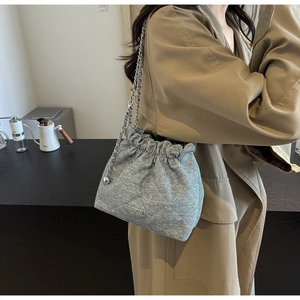 Detail of grey quilted bucket bag with silver chain and metal ball on beige coat