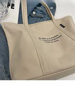 Close-up of beige canvas tote bag with black letter print on denim background