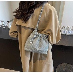 Quilted silver-grey bucket bag with metal chain strap and logo charm on a model