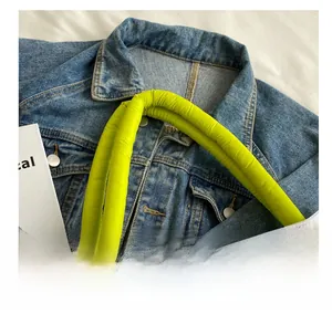 Detail of white tote bag featuring neon yellow padded handles and black metal carabiner