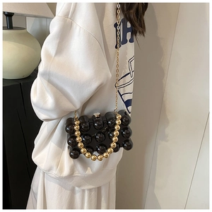 Dettaglio pochette in acrilico nero a bolle con manico a perle dorate e tracolla sottile