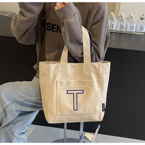 Close-up of canvas tote bag featuring a blue letter T patch and brand side label