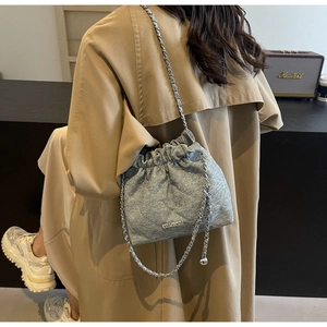 Detail of silver quilted bucket bag with chain strap and branding in a lifestyle setting