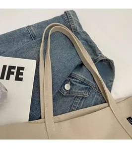 Detail of reinforced canvas handles on a beige tote bag with sturdy stitching