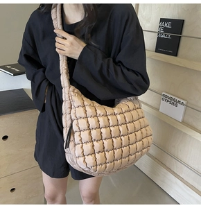 Close-up of beige quilted puffy tote bag on model shoulder with wood bookshelf background