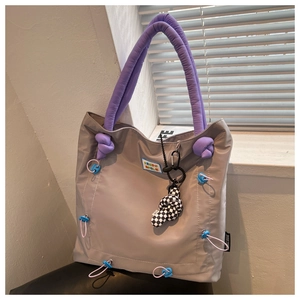 Detail of taupe nylon tote bag featuring purple padded handles and rainbow slogan label