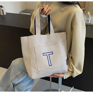 Detail of beige canvas tote bag featuring blue T embroidery and contrasting navy handles