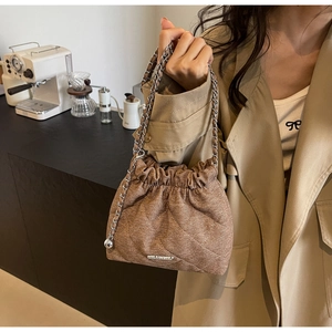 Detail of a brown quilted bucket bag featuring a drawstring closure and silver ball charm