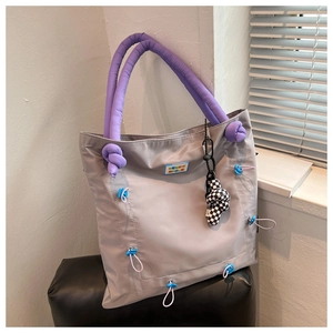 Close-up of a nylon tote bag with purple padded handles and checkerboard charm