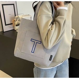 Detailed close-up of a large grey canvas tote bag with blue embroidered letter T
