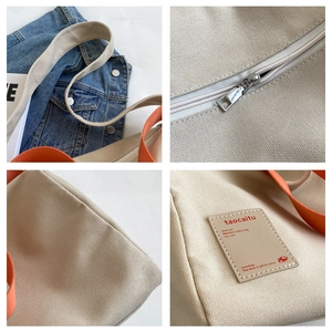 Detail view of khaki canvas tote with orange handles, metal zipper, and leather logo tag