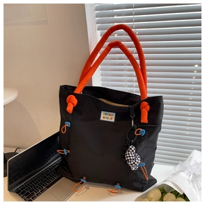 Close-up of black nylon tote bag with orange padded handles and checkerboard charm