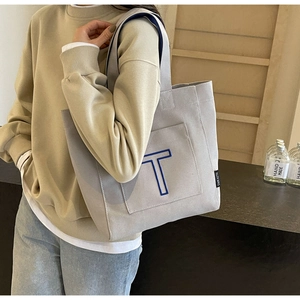 Detail of grey canvas tote bag with blue embroidered letter T and functional front pocket