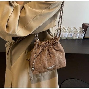Detail of a brown quilted drawstring bucket bag with silver chain and metal ball charm