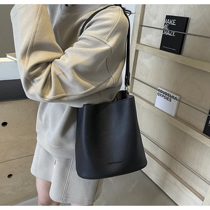 Detailansicht der schwarzen Eimer-Tasche aus genarbtem Leder mit elegantem Golddekor
