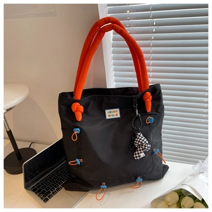 Detail of black nylon tote bag with orange padded handles and KEEDS SMILE patch