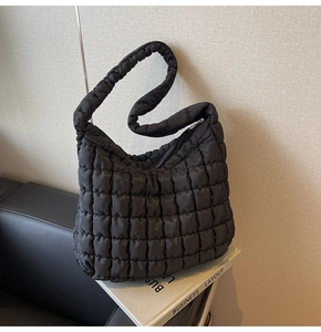 Detail of black quilted puffer hobo bag texture on a leather sofa with a book