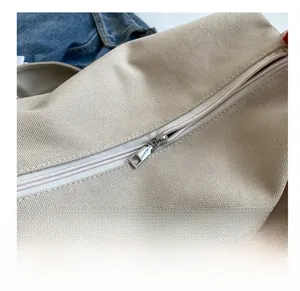 Detail of silver metal zipper and orange strap on beige canvas crossbody pillow bag