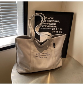 Detailed close-up of light grey canvas tote bag with black letter print and side label