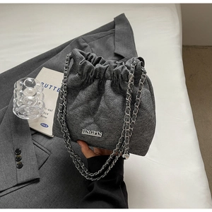 Detail of dark grey quilted bucket bag with silver metal chain and brand logo plaque