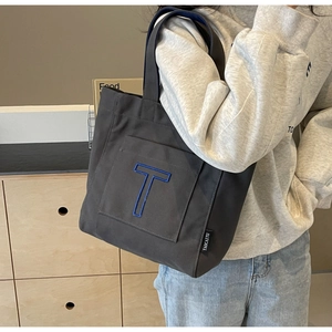 Detail of grey canvas tote bag featuring a large blue T graphic and brand side label