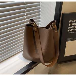 Detail der dunkelbraunen Eimer-Tasche aus Kieselleder mit breitem Gurt und Goldbeschlag