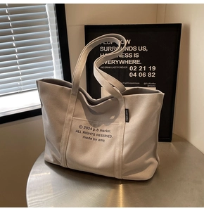 Detail of grey canvas tote bag with black letter print on a metal table surface
