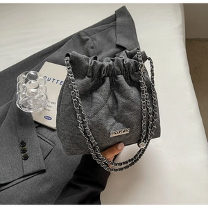Detailed view of grey quilted denim bucket bag with silver chain strap and drawstring closure