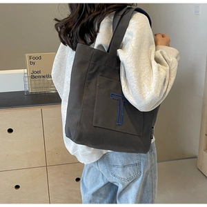 Detail of dark grey canvas tote bag featuring an embroidered blue T on the front pocket
