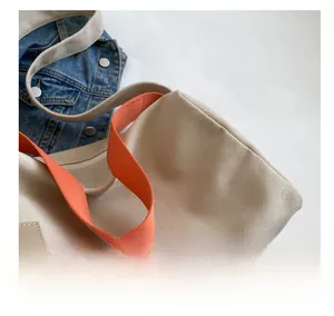 Detail of premium beige canvas pillow bag with vibrant orange strap and leather tag