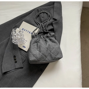 Close-up of grey quilted tweed bucket bag with silver chain strap on a blazer