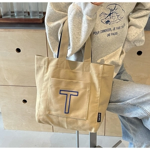Detailed view of khaki canvas tote bag with blue T embroidery and branded side label