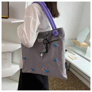 Close-up of gray nylon tote bag featuring purple padded straps and Keeds Smile patch