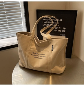 Close-up of beige canvas tote bag front pocket with minimalist letter printing