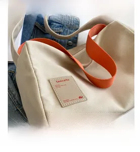 Detail shot of beige canvas bag with textured fabric and vibrant orange shoulder strap