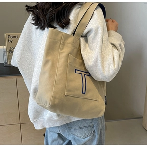 Detail of khaki canvas tote bag with blue T embroidery and side label on a shoulder
