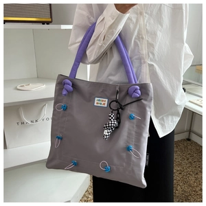 Detail of grey tote bag with purple handles featuring Keep Smile patch and rope knots