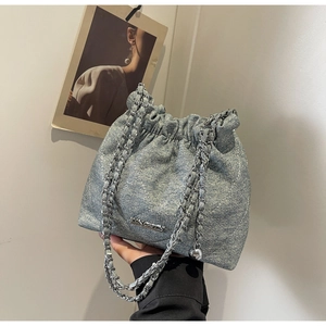 Close-up of quilted light blue denim bucket bag with metal chain strap and drawstring detail