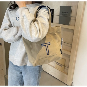 Detail of canvas tote bag with blue embroidered T and front pocket for daily commute