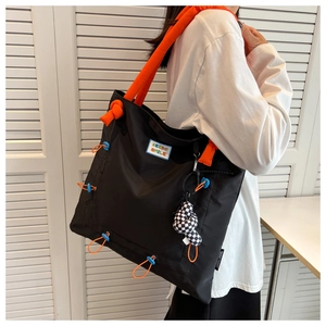 Detail of black nylon tote bag with orange padded strap and Keep Smile woven patch
