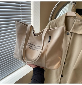 Detail showing high-capacity beige canvas tote bag with black letter print and side label