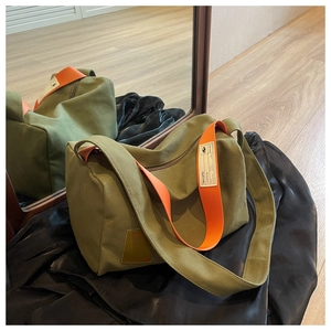 Detail of dark green canvas crossbody bag with wide orange contrast strap and logo tag