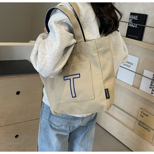 Side view of beige canvas tote bag with blue 'T' embroidery and interior lining detail