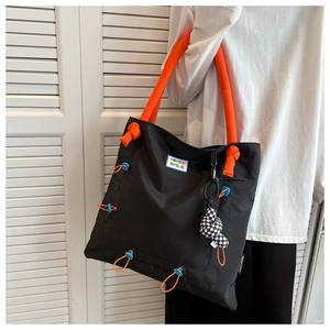 Nylon tote bag detail with orange padded handles and checkerboard charm decoration