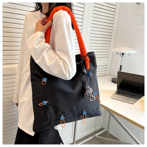 Detail of black nylon tote with bold orange straps and a checkered doll charm