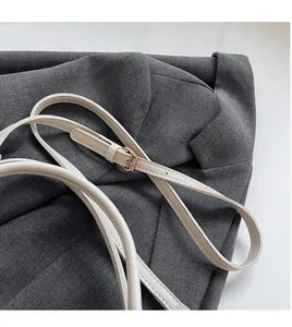 Detail of adjustable cream leather shoulder strap with gold buckle on gray blazer