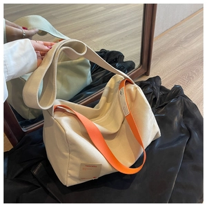 Detail of canvas pillow bag featuring a wide orange strap and leather logo patch