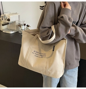 Close-up of beige canvas tote bag with black letter print and side brand label detail