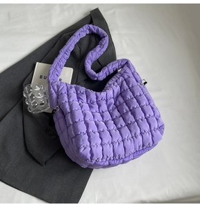 Detail of purple quilted puffer tote bag with soft padded straps on a textured background